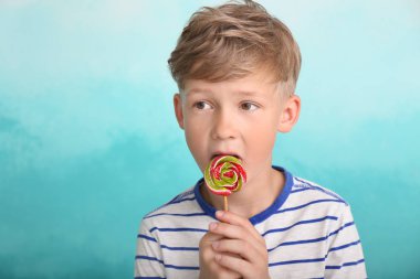 Renk arka plan üzerinde lolipop yiyen sevimli küçük çocuk