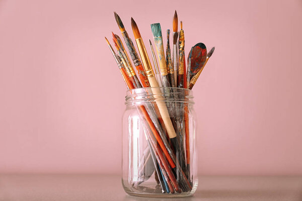 Стеклянная банка с набором кистей на столе на цветном фоне
