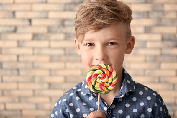 Cute little boy with lollipop near brick wall