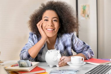 Kumbara masada olan genç Afrikalı-Amerikalı kadın. Tasarruf kavramı