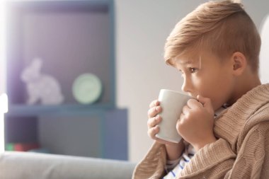 Sevimli küçük çocuk oturma kanepe evde sıcak kakao içecek fincan ile