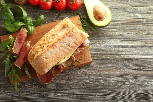 Tasty sandwich with prosciutto on wooden board