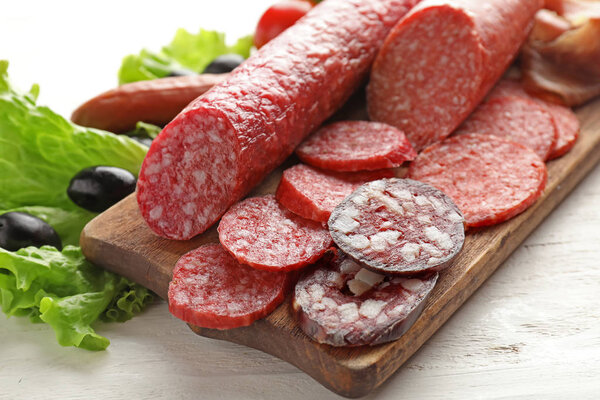 Wooden board with assortment of delicious sausages on light table
