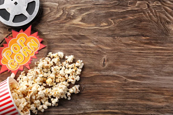Ahşap arka plan üzerinde lezzetli patlamış mısır ve film makarası ile kompozisyon