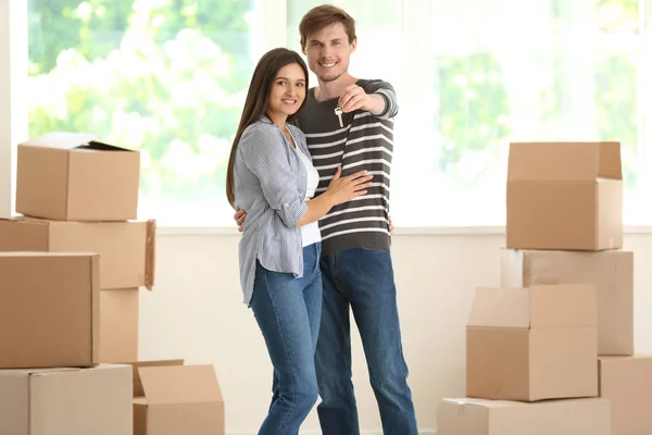 Young happy couple with key of their new house and moving boxes indoors