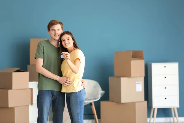 Young happy couple with key of their new house and moving boxes indoors