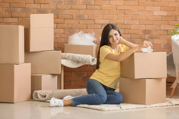 年轻快乐妇女与钥匙和移动的箱子坐在地毯在新的家 — 图库照片