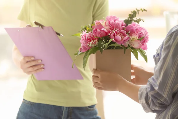 Woman receiving box with beautiful peony flowers from courier