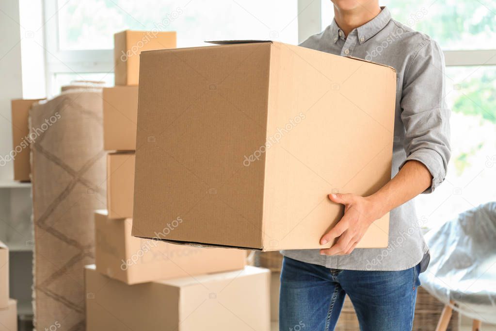 Young man with box indoors. Moving into new house