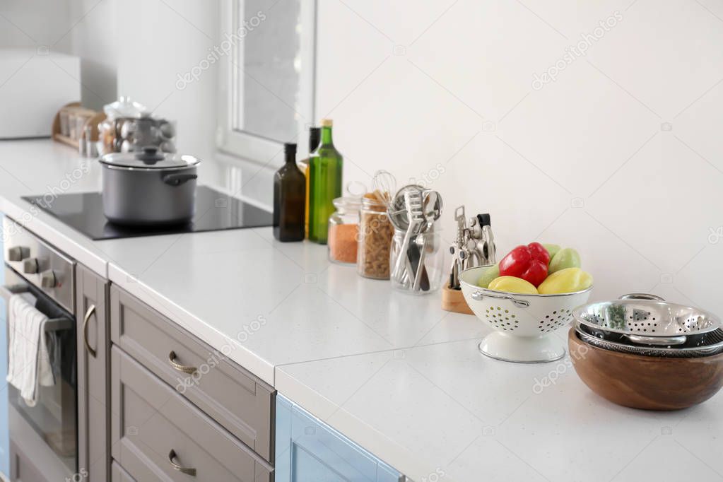 Cooking utensils with fresh vegetables and dishes on table in modern kitchen