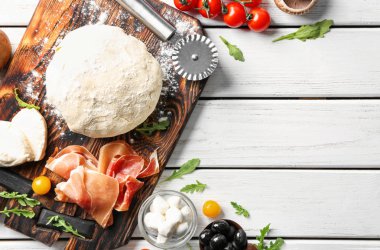 Çiğ hamur ve beyaz ahşap zemin üzerinde pizza için malzemeler