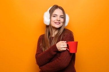 Güzel genç kadın sıcak kazaklı fincan çay renk arka plan üzerinde tutan