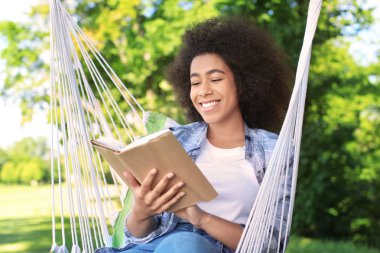 Güzel genç Afrikalı-Amerikalı kadın okuma kitabı hamak açık havada