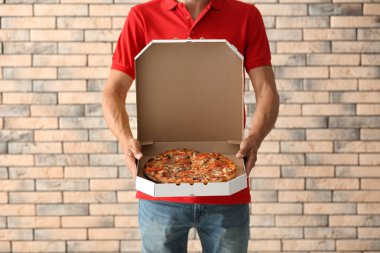 Lezzetli pizza kutusu tuğla duvara tutan genç adam. Gıda dağıtım hizmeti