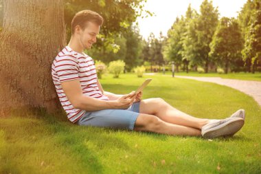 Genç adamla tablet Pc ağaç Parkı yakınında oturan