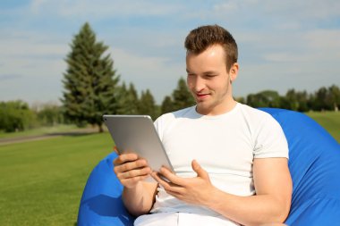 Genç adam açık havada fasulye çanta sandalyeye dinlenme Pc tablet