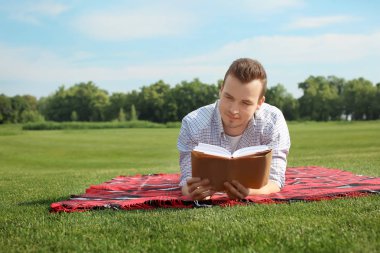 Genç adam açık havada ekose kitap okuma