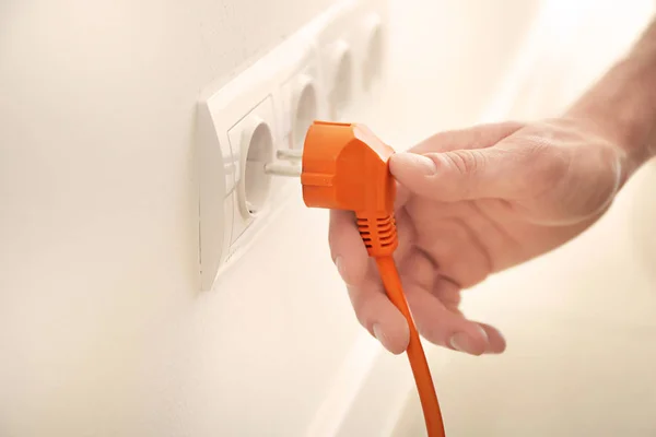 Male electrician inserting plug into socket in order to check its serviceability, closeup