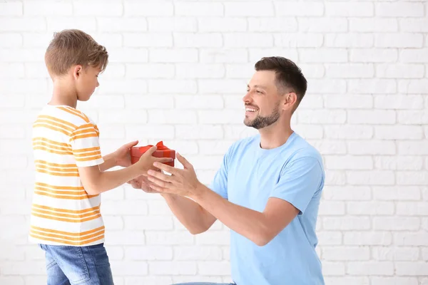 Man receiving gift for Father's Day from his son on light background
