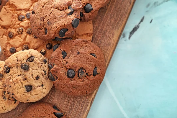 Wooden board with delicious chocolate chip cookies on table