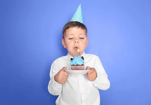 Menino Soprando Vela Aniversário Cupcake Contra Fundo Cor — Fotografia de Stock