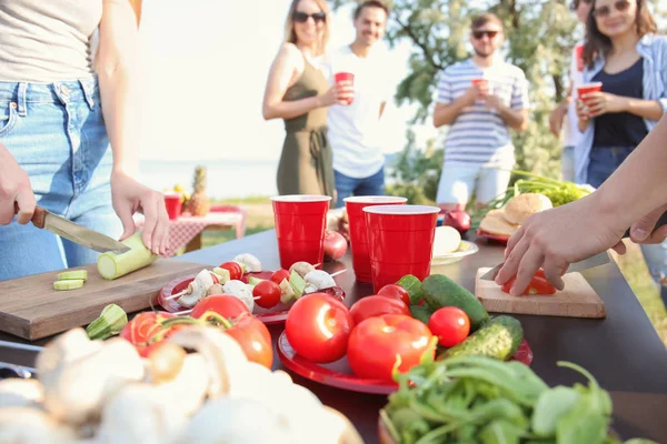 Young people cutting vegetables for barbecue party outdoors