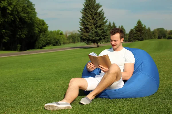 Young Man Reading Book While Sitting Bean Bag Chair Outdoors — Stock Photo, Image