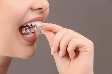 Woman putting occlusal splint in mouth on grey background, closeup clipart