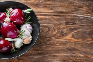 Taze soğan, sarımsak ve ahşap arka plan üzerinde otlar ile kase