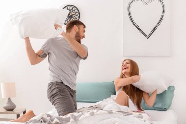 Mutlu genç çift yatakta evde oynarken yumuşak yastık ile