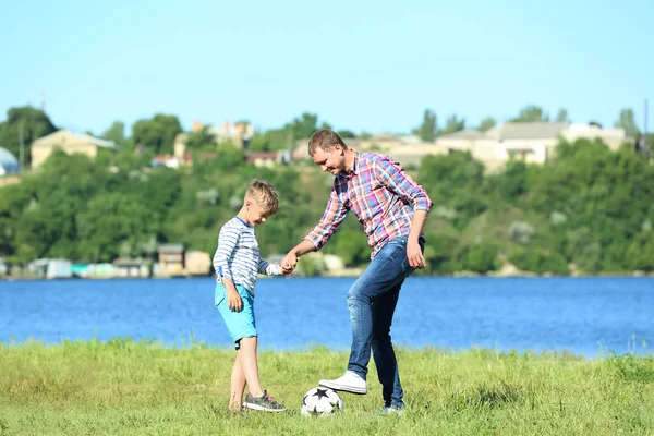 快乐的父亲和儿子在河边踢足球 — 图库照片