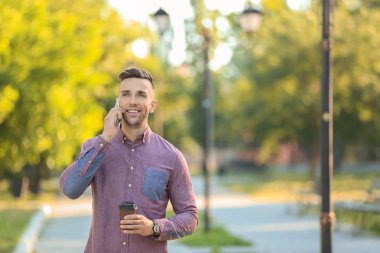 Yakışıklı adam cep telefonu üzerinde yeşil parkta yürürken konuşurken