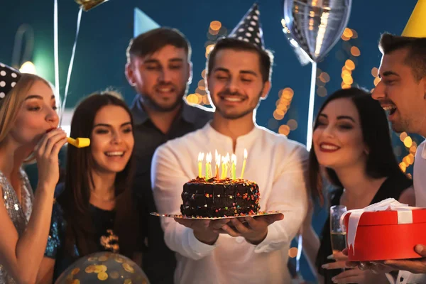 Young man with tasty cake and his friends at birthday party in club