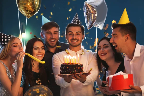 Young man with tasty cake and his friends at birthday party in club