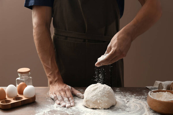 Man sprinkling dough with flour on color background