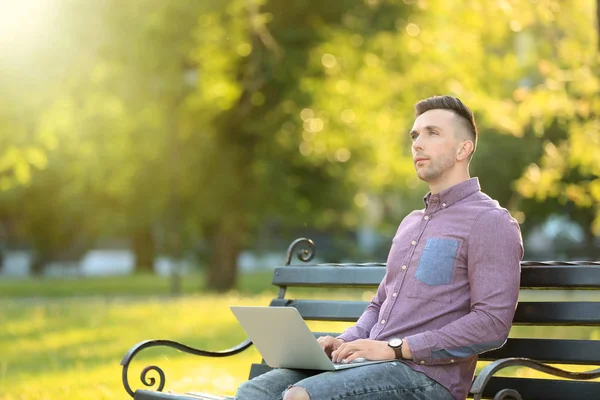 Handsome man with laptop resting on bench in park