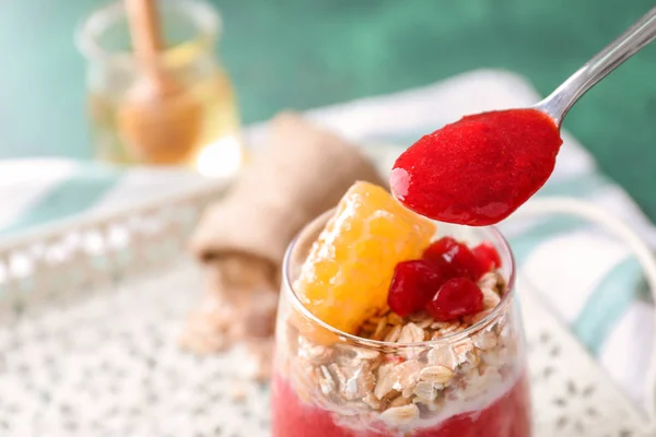 Spoon with berry jam and tasty oatmeal dessert in glass on table, closeup