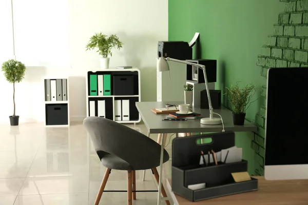 Stylish workplace with notebooks and lamp on table near color wall in office