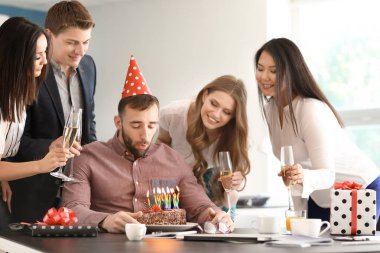 Genç adam onun Doğum günü pastası Office meslektaşları ile mum dışarı üfleme