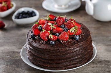 Çilek ve ahşap masa üzerinde yaban mersini ile dekore edilmiş lezzetli çikolatalı kek