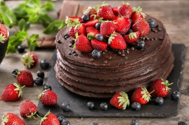 Çilek ve ahşap masa üzerinde yaban mersini ile dekore edilmiş lezzetli çikolatalı kek