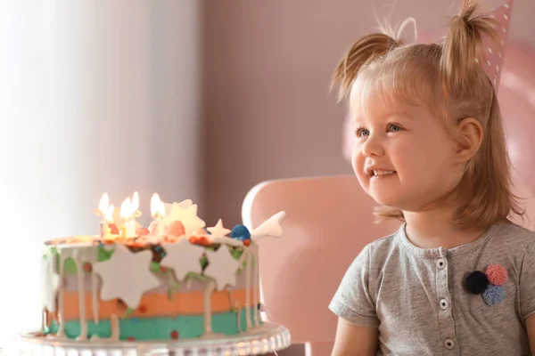 Cute little girl with birthday cake sitting on chair in room