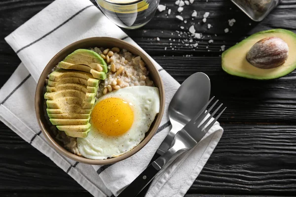 Bowl with delicious oatmeal, egg and avocado on wooden table
