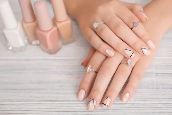Young woman with stylish manicure and nail polishes on wooden background