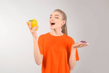 Genç kadın tatlı ve biber arasında seçim yapma gri arka plan üzerinde. Diyet gıda kavramı