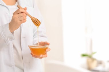 Kepçe ve bal ile kase üzerinde arka plan bulanık tutan kadın güzellik uzmanı