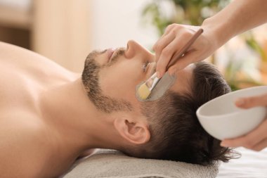 Adamın yüzünü spa salonda kozmetik maskesi uygulayarak güzellik uzmanı