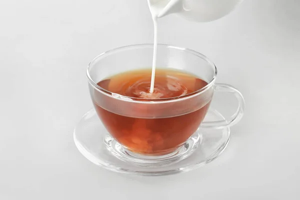 Adding milk to delicious tea on light background