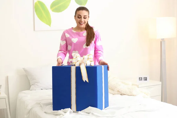 Beautiful young woman with big gift box in bedroom