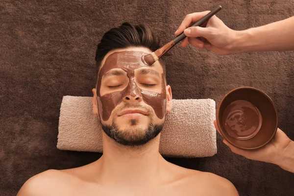 Beautician applying cosmetic mask on man's face in spa salon